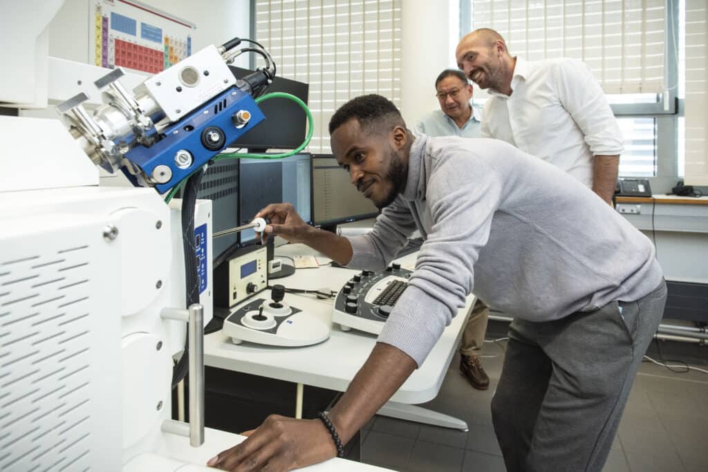 Cette image montre deux individus dans un laboratoire, concentrés sur l’utilisation d’un équipement scientifique complexe pour analyser des échantillons ou des données. L’environnement est professionnel et bien équipé, indiquant un cadre de recherche ou d’analyse sérieux.